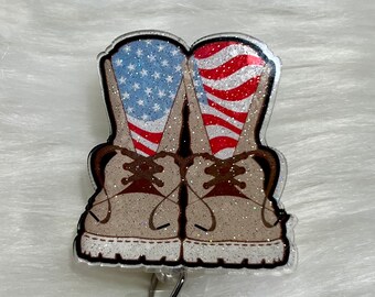 Op de afbeelding: Een transparante plastic badgehouder met een ontwerp van twee bruine laarzen met Amerikaanse vlagontwerpen op de bovenkant van de laarzen. De badgehouder heeft een transparante, intrekbare rol van plastic.