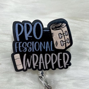 May include: Black and white badge reel with glitter accents. The badge reel features a white bandage with a black outline and the text "Pro-fessional Wrapper".