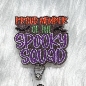 May include: Purple and black glitter badge holder with the text "Proud Member of the Spooky Squad" and two black bats.