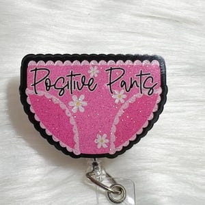 May include: Pink glitter badge holder with a black border and white daisies. The badge holder is shaped like a pair of underwear and says "Positive Pants" in black lettering.