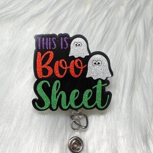 May include: A black and green glitter badge holder with the text "This is Boo Sheet" and two white ghosts with black eyes.