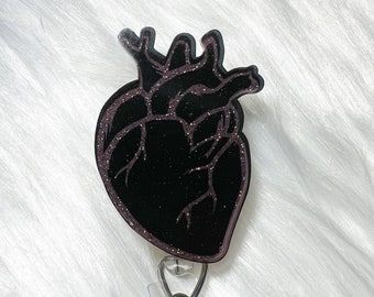 Puede incluir: Porta credenciales en forma de corazón negro con purpurina y un carrete retráctil de plástico transparente.