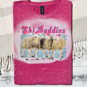 May include: A pink t-shirt with a bleached design featuring three sheep with flower crowns and the text "Shi Buddies".