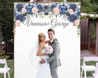 May include: A white backdrop with a floral design in shades of blue and pink. The text "Vanessa & George" is written in black cursive script. A bride and groom are standing in front of the backdrop.