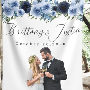 Pu&ograve; includere: Uno sfondo bianco per matrimoni con una ghirlanda di fiori blu in alto. Il testo "Brittany & Justin" e "October 20, 2020" &egrave; stampato sotto la ghirlanda. Una foto di una coppia &egrave; nella met&agrave; inferiore dello sfondo.