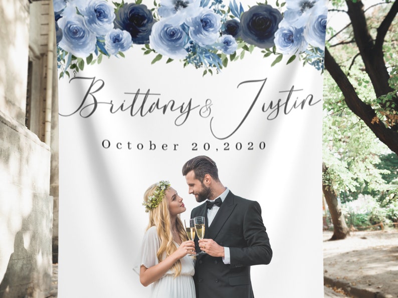 Pu&ograve; includere: Uno sfondo bianco per matrimoni con una ghirlanda di fiori blu in alto. Il testo "Brittany & Justin" e "October 20, 2020" &egrave; stampato sotto la ghirlanda. Una foto di una coppia &egrave; nella met&agrave; inferiore dello sfondo.