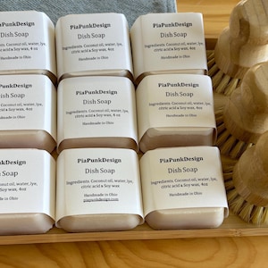 May include: Nine bars of handmade dish soap in a wooden tray. Each bar is labelled "PiaPunkDesign Dish Soap" and lists the ingredients: coconut oil, water, lye, citric acid & soy wax, 4 oz. The bars are handmade in Ohio.