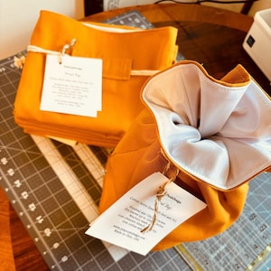 May include: Mustard-colored cotton fabric lined with white fabric, drawstring bag. The bag is tied with a natural twine and a tag. The tag reads "PunkDesign" and includes care instructions. The finished size is 15x10 inches.