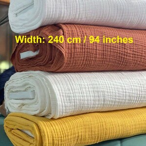 May include: A stack of four fabric bolts featuring a crinkled, multi-layered texture. The colours include white, terracotta, white, and mustard yellow. The text on the terracotta bolt reads: Width: 240 cm / 94 inches. The fabric is rolled.