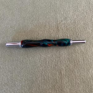 Può includere: Primo piano di un uncinetto in legno nero, verde e rosso con estremità in metallo argentato.