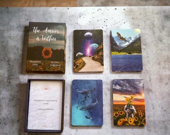 May include: A set of 7 cards with colorful images and a small guidebook. The cards feature images of a sunflower, a galaxy, a mountain lake, a shark, a sunflower field, and a person with a sunflower head. The guidebook has the text "Metaphoric associative cards" and "Little guidebook". The cards are titled "The Answer is Within" and are by Yulia Naguseva.