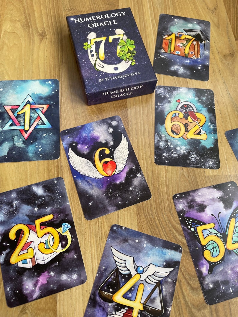 May include: A set of tarot cards with a galaxy background and gold numbers. The cards feature various symbols, including a horseshoe, a house, a butterfly, a heart, a scale, and a suitcase. The cards are part of a numerology oracle deck.