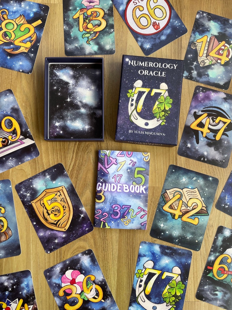 May include: A numerology oracle deck with a guidebook. The cards feature a galaxy background with numbers and symbols. The guidebook has a galaxy pattern with numbers printed on the cover.