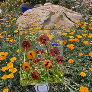 May include: A decorative night light featuring a floral design. The glass panel displays orange, brown, and yellow flowers with green leaves and accents. The night light has a white base and is set against a backdrop of yellow flowers.
