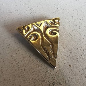 May include: A gold-toned triangular brooch with an intricate, embossed design.