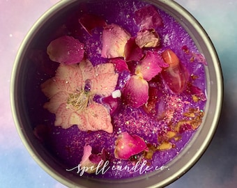 May include: Purple candle with dried flowers and glitter. The candle is in a silver tin with the text "spell candle co."