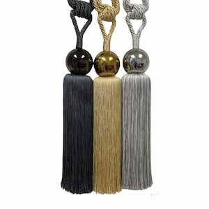 May include: Three tassel tiebacks with decorative balls. The tiebacks are black, gold, and silver.