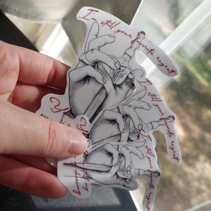 May include: Three white stickers with black and gray illustrations of hands holding a knife. The text on the stickers reads "I'm still your favorite regret".