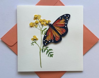 May include: A handmade greeting card featuring a paper quilled butterfly with orange, red, and black wings. The butterfly is perched on a yellow flower with green leaves. The card is white with a cream colored envelope.
