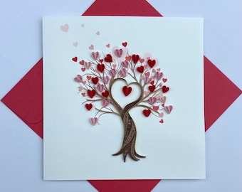 May include: A handmade card featuring a brown paper quilled tree with pink and red hearts for leaves. The tree has a large heart shape in the center, formed by its branches. The card is perfect for Valentine's Day or any occasion to express love.
