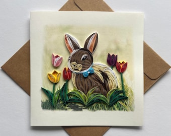 May include: A handmade paper quilling card featuring a brown bunny with a blue bow tie surrounded by colorful tulips. The card is perfect for Easter or a spring birthday.