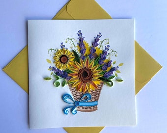 May include: A handmade greeting card featuring a paper quilling design of a basket of sunflowers and lavender. The basket is brown with a blue ribbon.