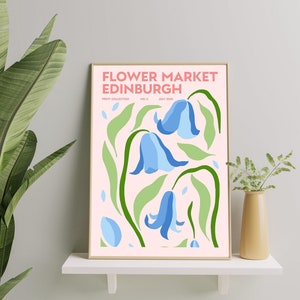 May include: A pink poster with the text "FLOWER MARKET EDINBURGH" in white and pink lettering. The poster features a stylized illustration of three blue bell flowers with green leaves on a pink background.