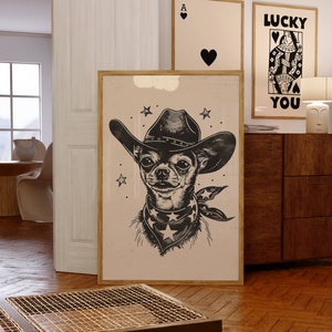 May include: A framed art print featuring a black and white illustration of a Chihuahua wearing a cowboy hat and bandana with stars. Two other framed prints are visible in the background, one with a heart and the other with the text "LUCKY YOU".