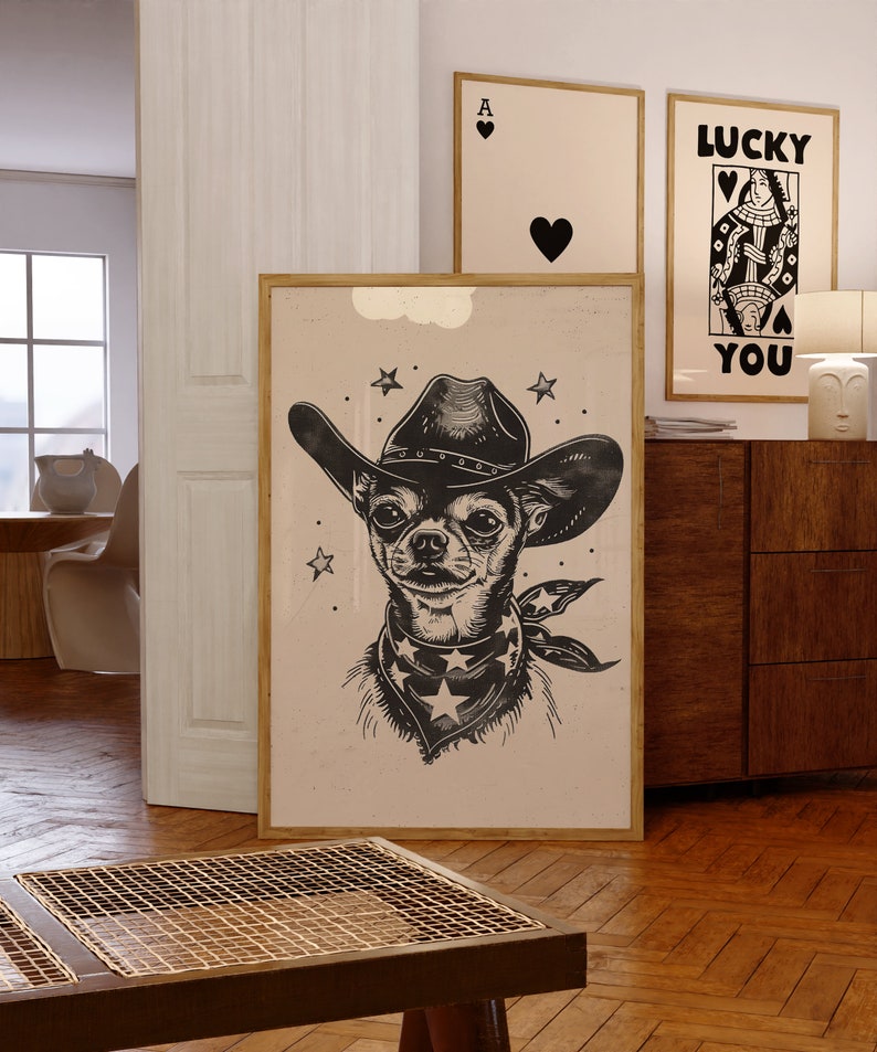 May include: A framed art print featuring a black and white illustration of a Chihuahua wearing a cowboy hat and bandana with stars. Two other framed prints are visible in the background, one with a heart and the other with the text "LUCKY YOU".