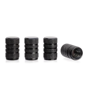 May include: Four black tire valve stem caps. The caps are cylindrical with a textured, ridged design. Three caps are upright, while one is lying on its side, revealing the internal threads.