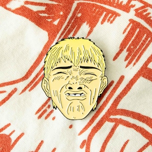 Può includere: Uno spillo in smalto giallo con un personaggio dei cartoni animati con un'espressione di angoscia. Il personaggio ha i capelli biondi e indossa una camicia bianca.