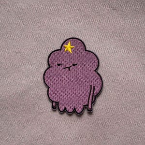 May include: Purple embroidered patch of a cartoon character with a yellow star on its head. The character has a grumpy expression and is shaped like a cloud.