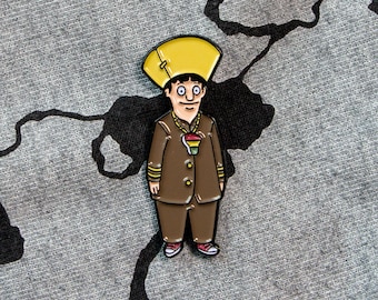 Könnte beinhalten: Eine Emaille-Anstecknadel mit einem Comic-Charakter, der einen gelben Hut und einen braunen Anzug mit einer Regenbogenkette trägt. Der Charakter hat einen braunen Schnurrbart und einen überraschten Gesichtsausdruck.