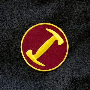 May include: A red circle patch with a yellow hammer design. The hammer is stylized and has a rounded head.