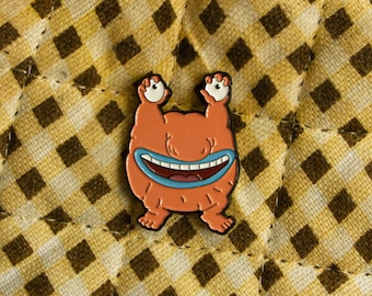 May include: Orange cartoon character with a big smile and two eyes. The character is standing on a brown and white checkered background.
