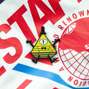 May include: A yellow triangle-shaped pin with a black outline and a single eye. The pin has a black bow tie and black legs. The pin is on a white and red background with the text "WORLD RENOWN" and "GRAVITY FALLS" visible.