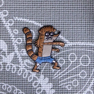 May include: A brown and gray cartoon raccoon with a blue jean shorts, a bushy tail, and an angry expression. The raccoon is in a fighting stance with its arms raised.
