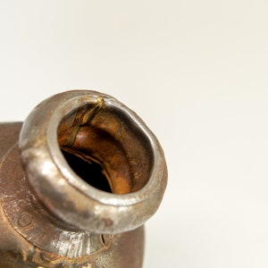 K&ouml;nnte beinhalten: Nahaufnahme eines rostigen Metallkatalysators mit einer runden &Ouml;ffnung. Der Katalysator besteht aus Metall und hat eine raue, strukturierte Oberfl&auml;che.