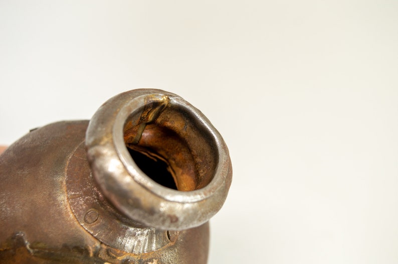 K&ouml;nnte beinhalten: Nahaufnahme eines rostigen Metallkatalysators mit einer runden &Ouml;ffnung. Der Katalysator besteht aus Metall und hat eine raue, strukturierte Oberfl&auml;che.