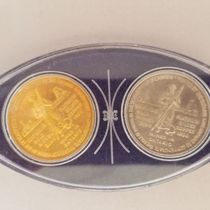 Könnte beinhalten: Zwei goldfarbene Münzen in einem durchsichtigen Plastiketui. Die Münzen sind Gedenkmünzen und zeigen ein Design einer Person, die eine Spitzhacke und einen Karren hält. Der Text auf den Münzen lautet "MINTED BY THE ONTARIO GOVERNMENT TO COMMEMORATE THE ROLE OF MINING IN THE DEVELOPMENT OF CANADA" und "PLATINUM SILVER COPPER IRON NICKEL ZINC MINED IN ONTARIO".