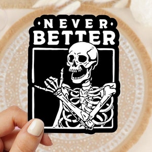 May include: Black and white sticker featuring a skeleton giving a "hang loose" gesture. The sticker has the text "NEVER BETTER" in a bold white font.