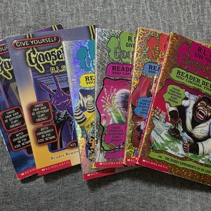 Puede incluir: Una colección de cinco libros Give Yourself Goosebumps de R.L. Stine, con portadas ilustradas coloridas y detalles en papel holográfico. Cada libro de bolsillo muestra varios gráficos de terror, la marca Scholastic y texto.