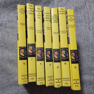May include: A collection of eight yellow paperback books with black text and illustrations. The books are Nancy Drew Mystery Stories. The titles include "The Message in the Hollow Oak", "The Clue in the Diary", "The Mystery at Lilac Inn", "The Secret in the Old Attic", "The Haunted Snowboat", and "The Password to Larkspur Lane".