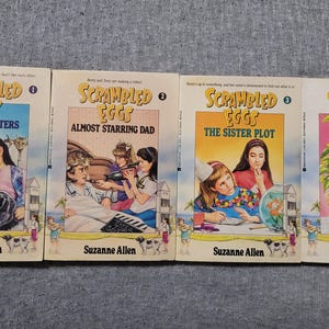 May include: A set of four paperback books with colorful covers featuring illustrations of girls and the title "Scrambled Eggs". Each book has a different title: "Suddenly Sisters", "Almost Starring Dad", "The Sister Plot", and "Berry and the Beanstalk".