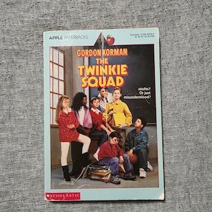May include: A paperback book titled "The Twinkie Squad" by Gordon Korman. The cover features a group of diverse young people. The book is part of the Apple Paperbacks series and published by Scholastic.