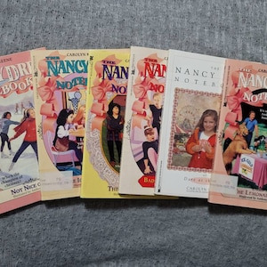 May include: A collection of six paperback books with pink covers featuring the Nancy Drew Notebooks series. The books are titled "Not Nice to Cheaters", "The Ice Cream Mystery", "The Bad Luck Charm", "Dare at the Carnival", and "The Lemonade Raid".
