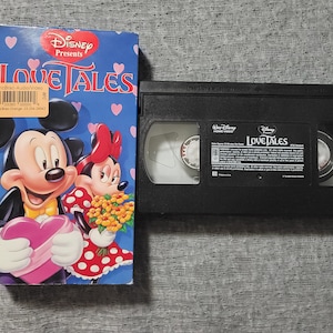 May include: A VHS tape of Disney Presents Love Tales featuring Mickey Mouse and Minnie Mouse on the cover. The tape is in a black case with the title "Love Tales" printed on the front.