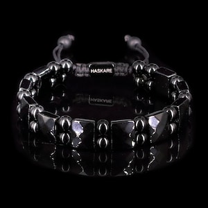 Könnte beinhalten: Schwarzes Onyx-Armband mit quadratischem Perlenmuster und einer schwarzen Schnur mit dem Wort "HASKARE" in silbernen Buchstaben.