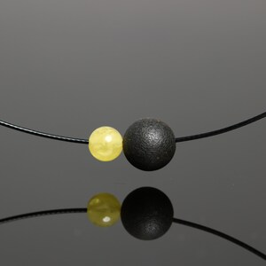 May include: A black cord necklace with a yellow and black bead. The yellow bead is on the left and the black bead is on the right.