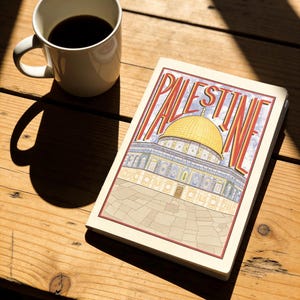 Pode incluir: Uma caneca de cerâmica branca cheia de café escuro está ao lado de um caderno com a palavra "PALESTINE" em letras vermelhas e amarelas. O caderno apresenta uma ilustração de um edifício com cúpula dourada. Os objetos repousam sobre uma superfície de madeira.